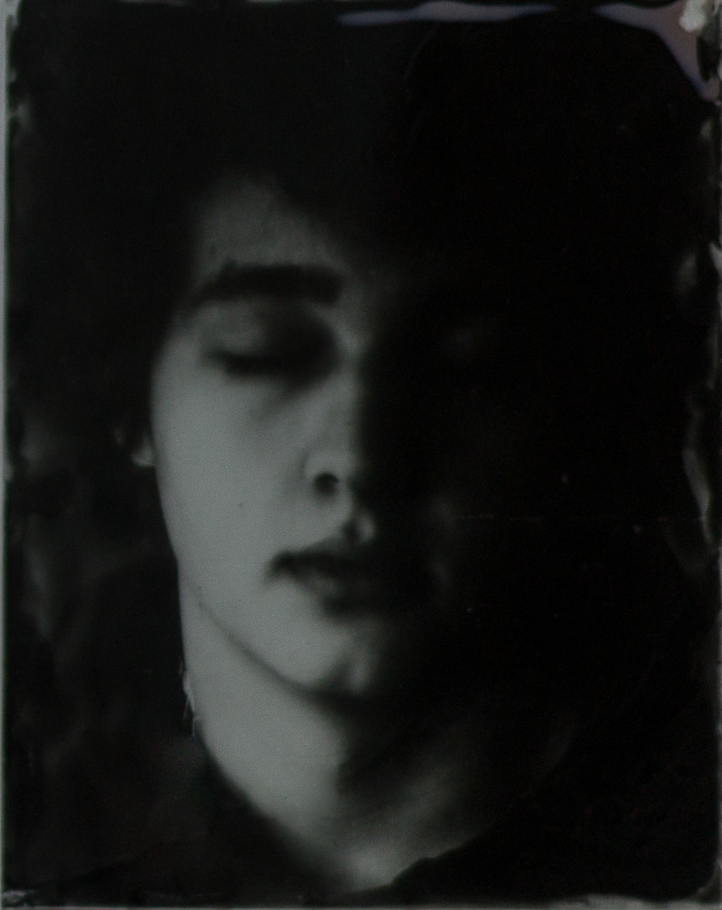Black-and-white portrait with closed eyes, half the face in shadow and irregular dark edges