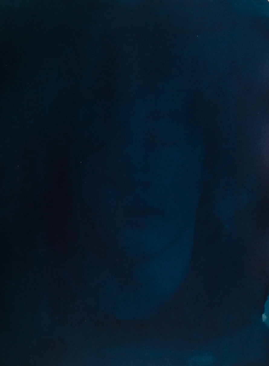 A face emerging faintly from a deep blue photographic print