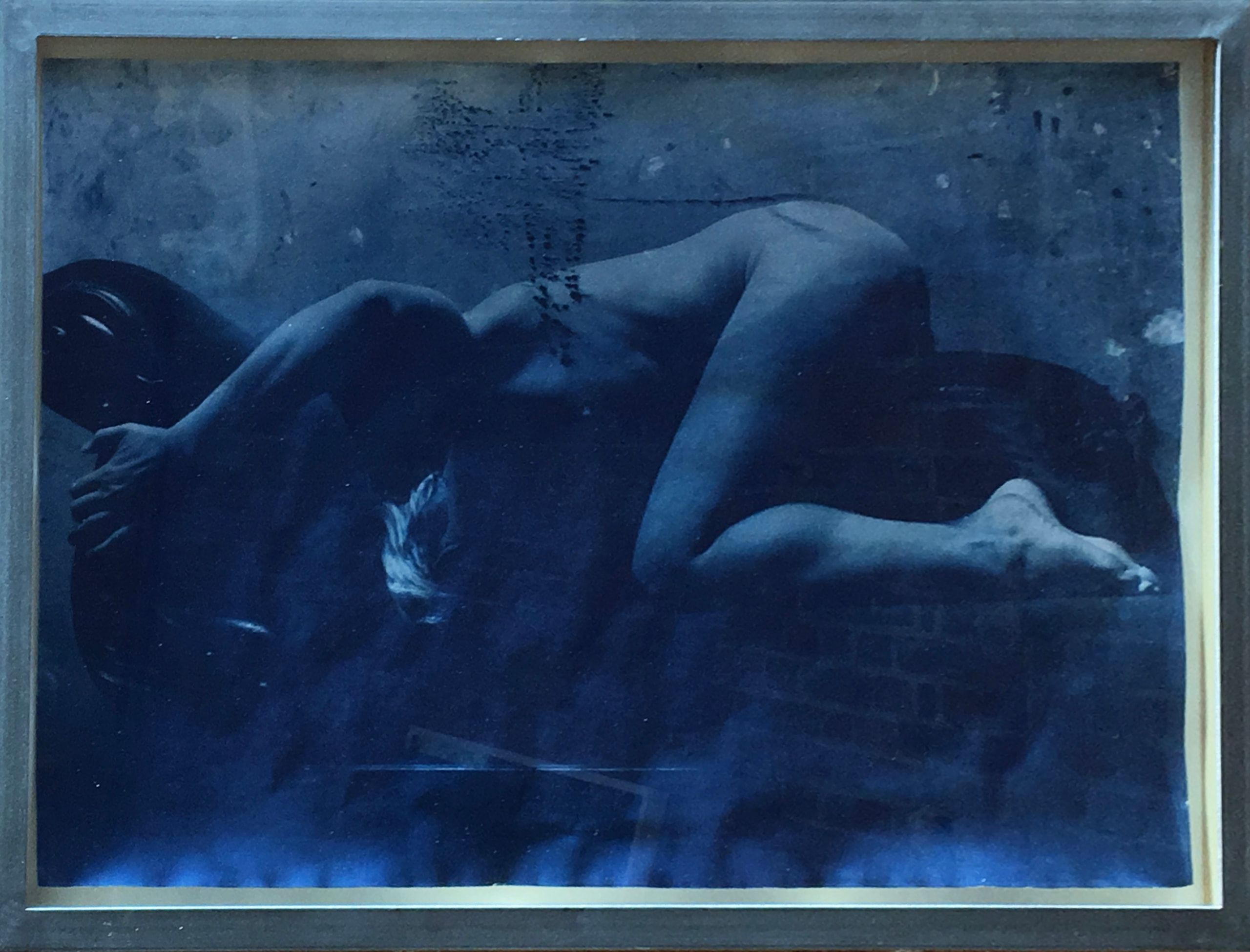 A framed blue-toned image of a curled reclining figure