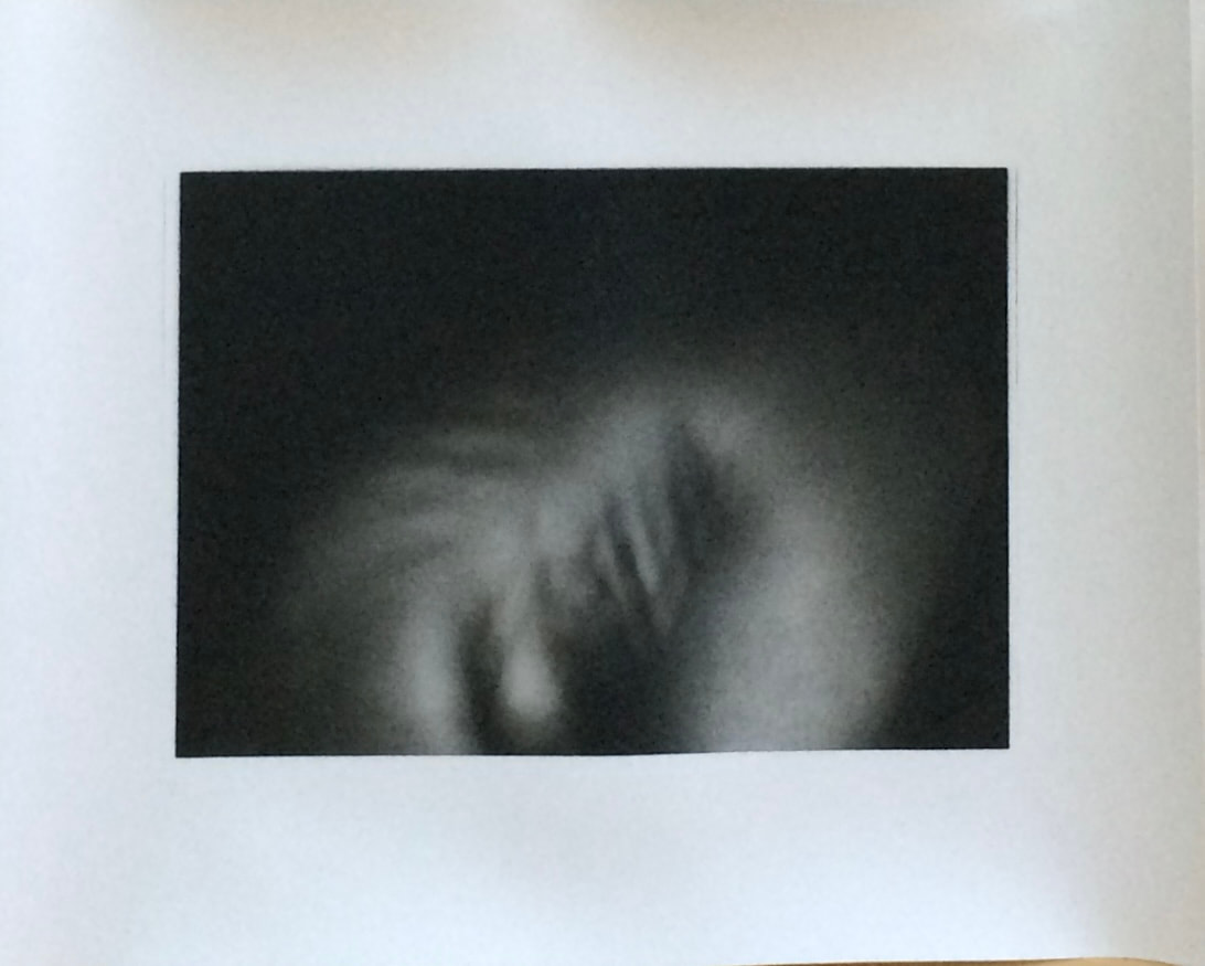 A softly blurred monochrome body study against a dark background, mounted on white paper