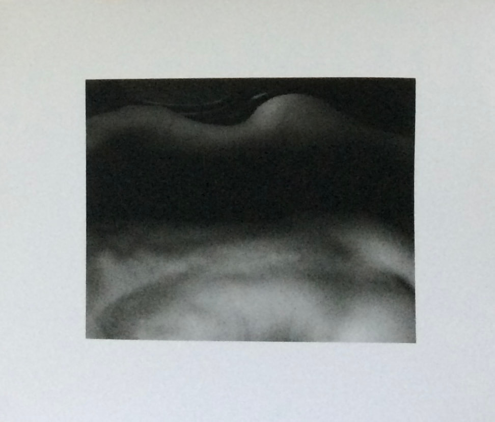 A soft-focus monochrome study of a reclining body, mounted on white paper