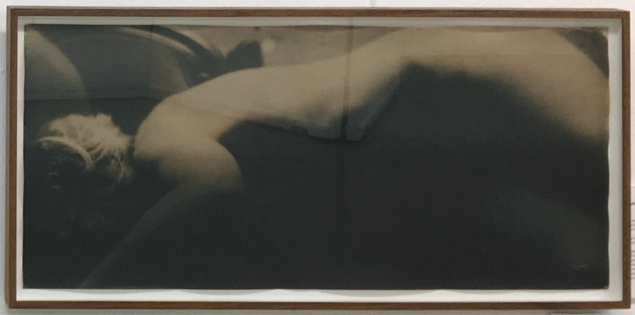A framed horizontal photograph of a reclining figure against a dark background