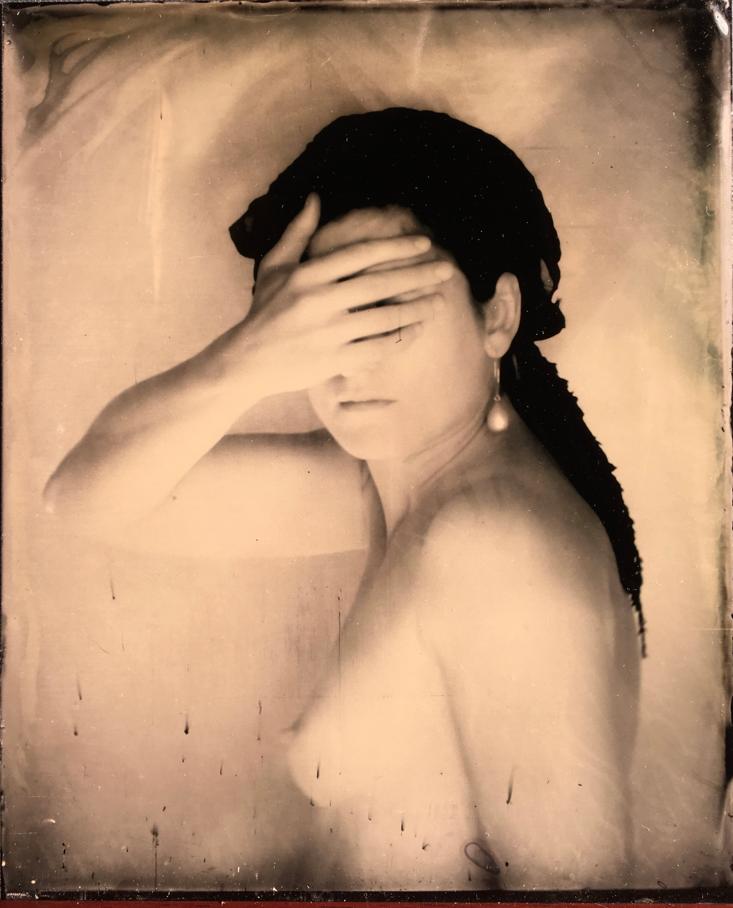 Sepia-toned portrait with a hand covering the eyes, a bare shoulder and dark textured edges