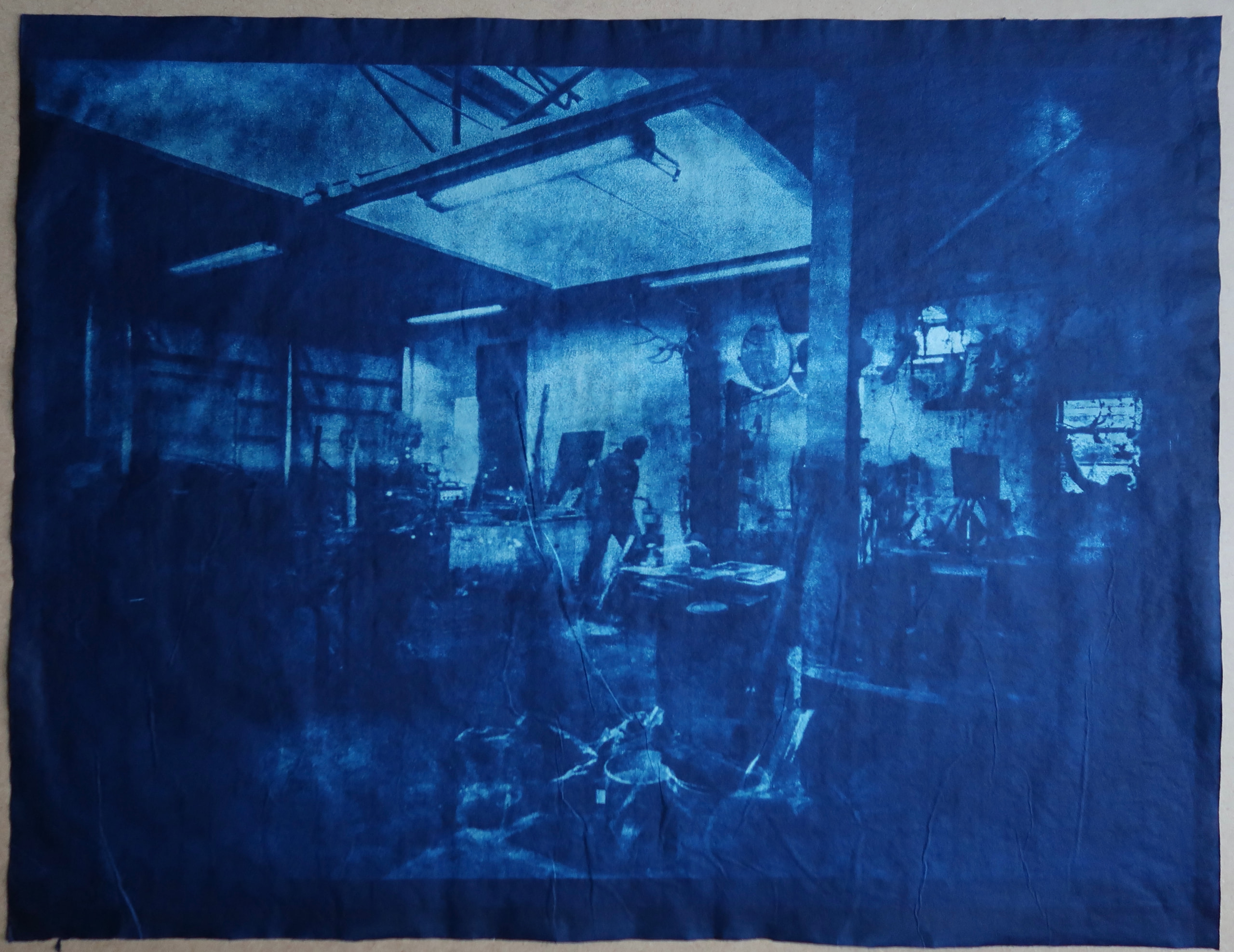 Deep blue image of a studio interior with roof beams, worktables and sculptural forms