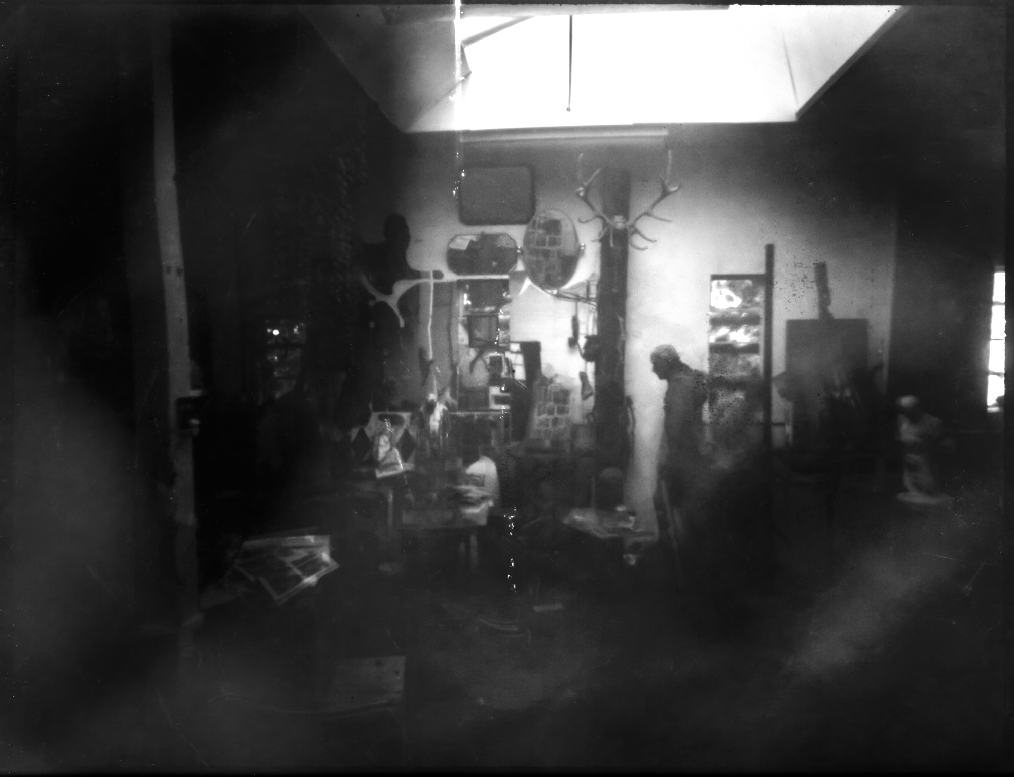 Dim sculptor’s studio with a bright skylight, shelves and a blurred standing figure