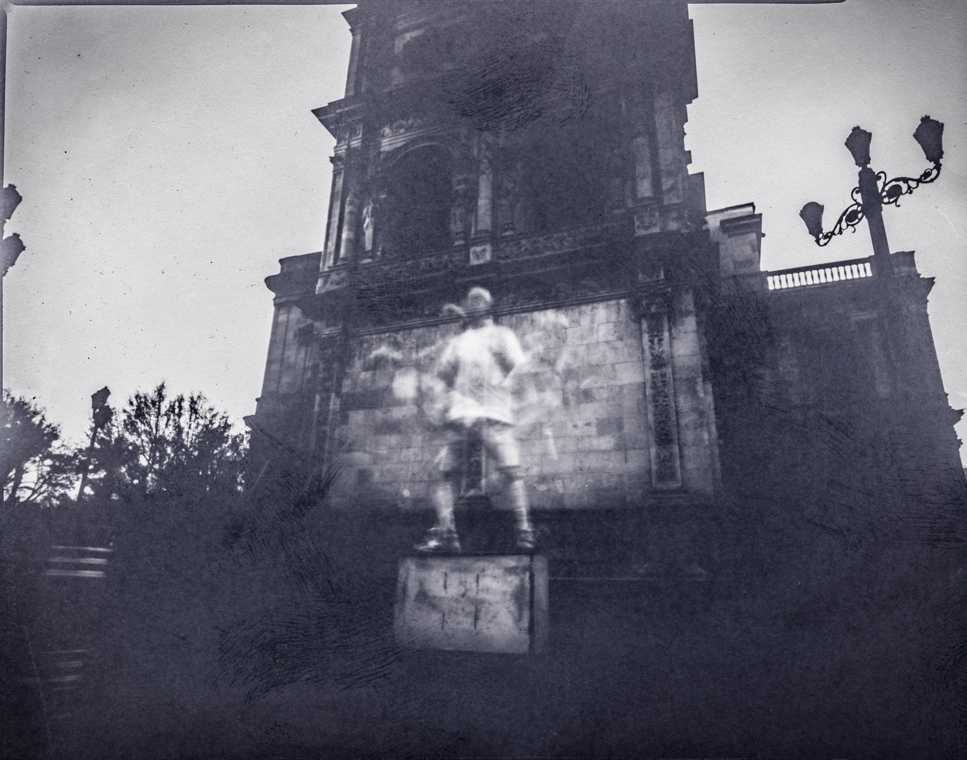Blurred pale figure in front of an ornate stone monument and street lamps