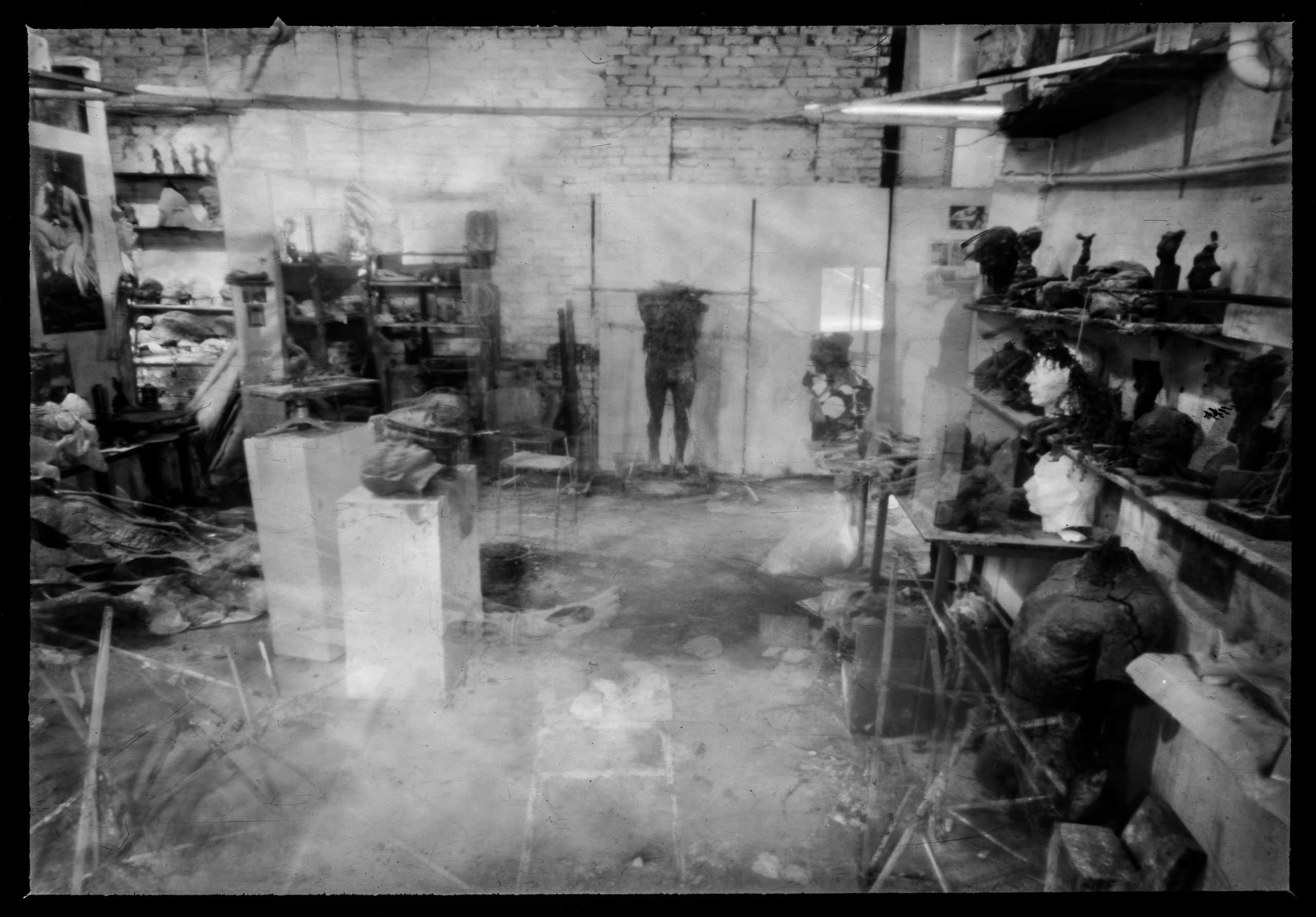 Black-and-white workshop interior with shelves of sculpted heads and translucent overlapping forms