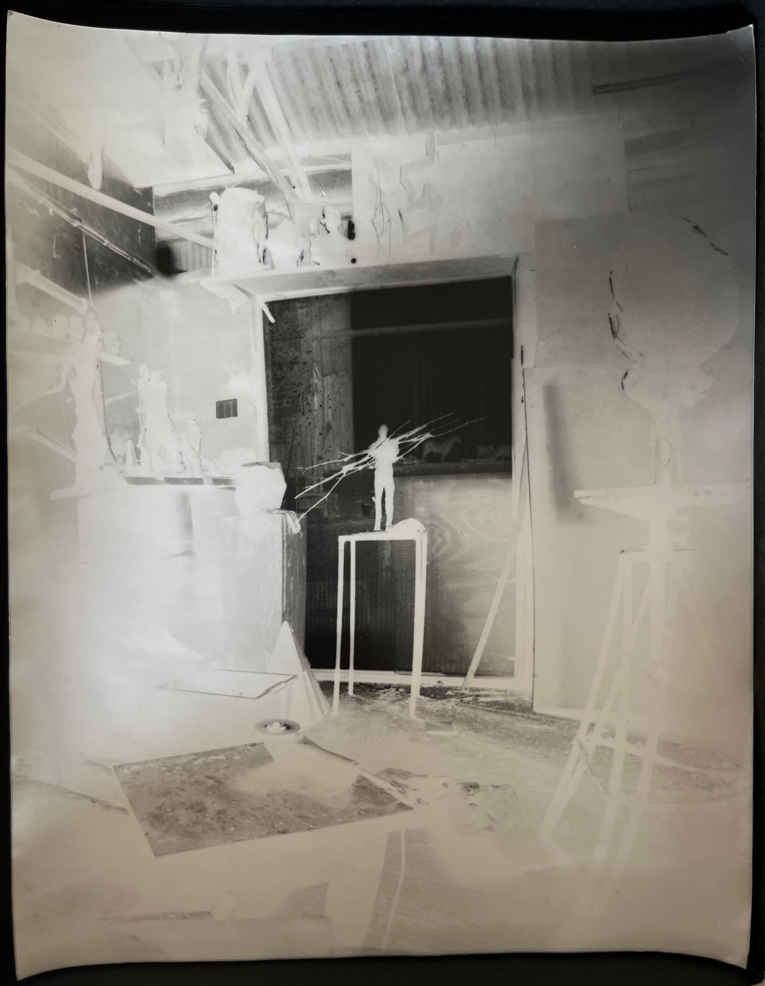 Negative-toned studio interior with a small figure on a plinth framed by a dark doorway