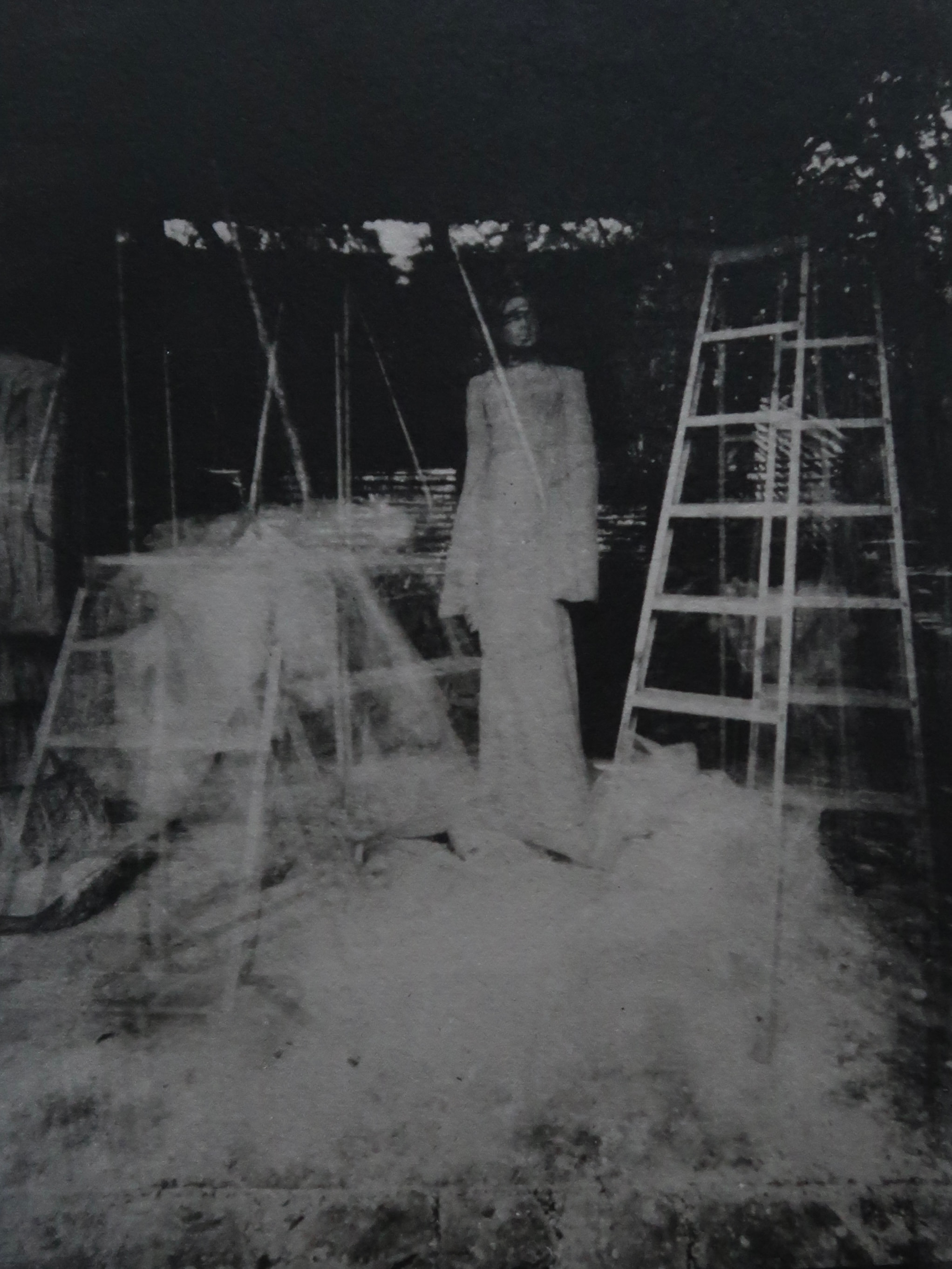 Negative-toned studio photograph with a ladder and pale overlapping sculptural forms