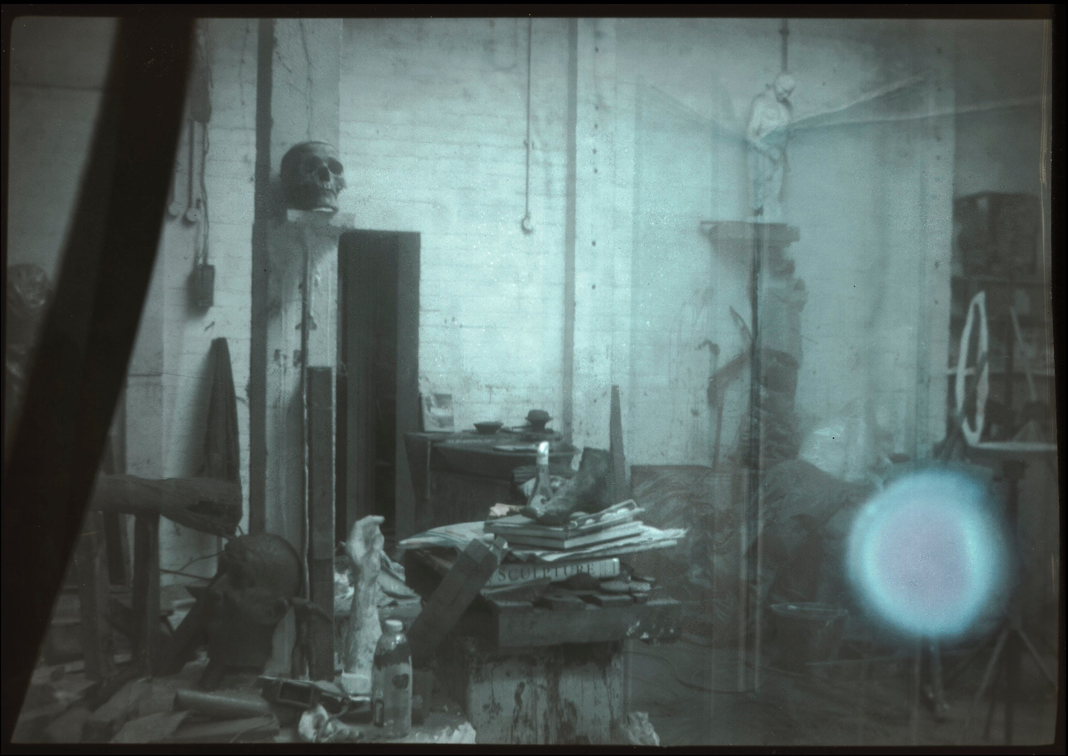 Studio interior with sculptures on tall stands and a pale circular light in the foreground