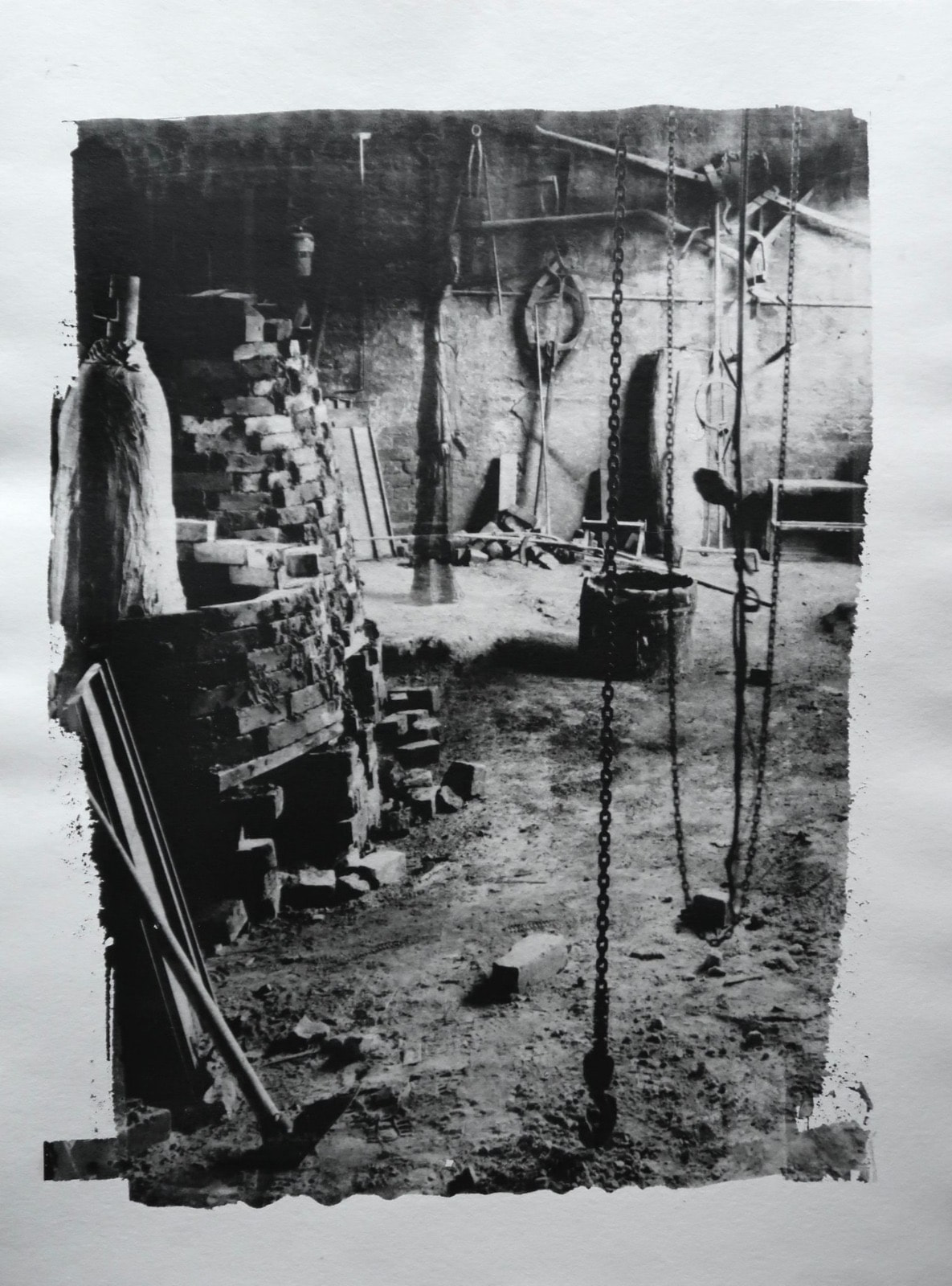 Black-and-white workshop interior with hanging tools and sculptural forms, bordered by irregular dark edges